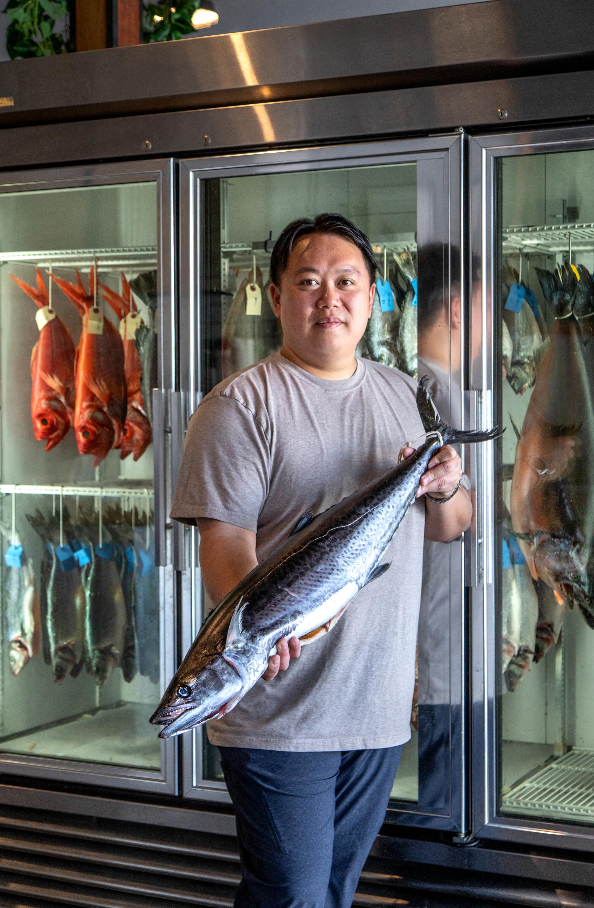 A man holds a whole mackerel at a fish market.