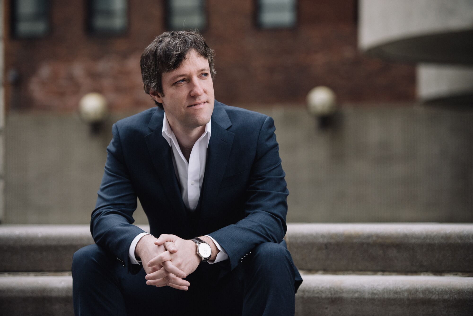 Milwaukee Symphony Orchestra conductor Yaniv Dinur sits on stairs.