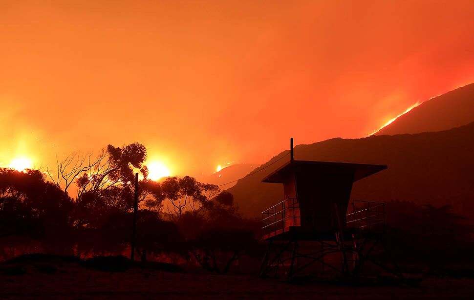 A lifeguard tower is silhouetted by the fire above Pacific Coast Highway as flames head toward the ocean.
