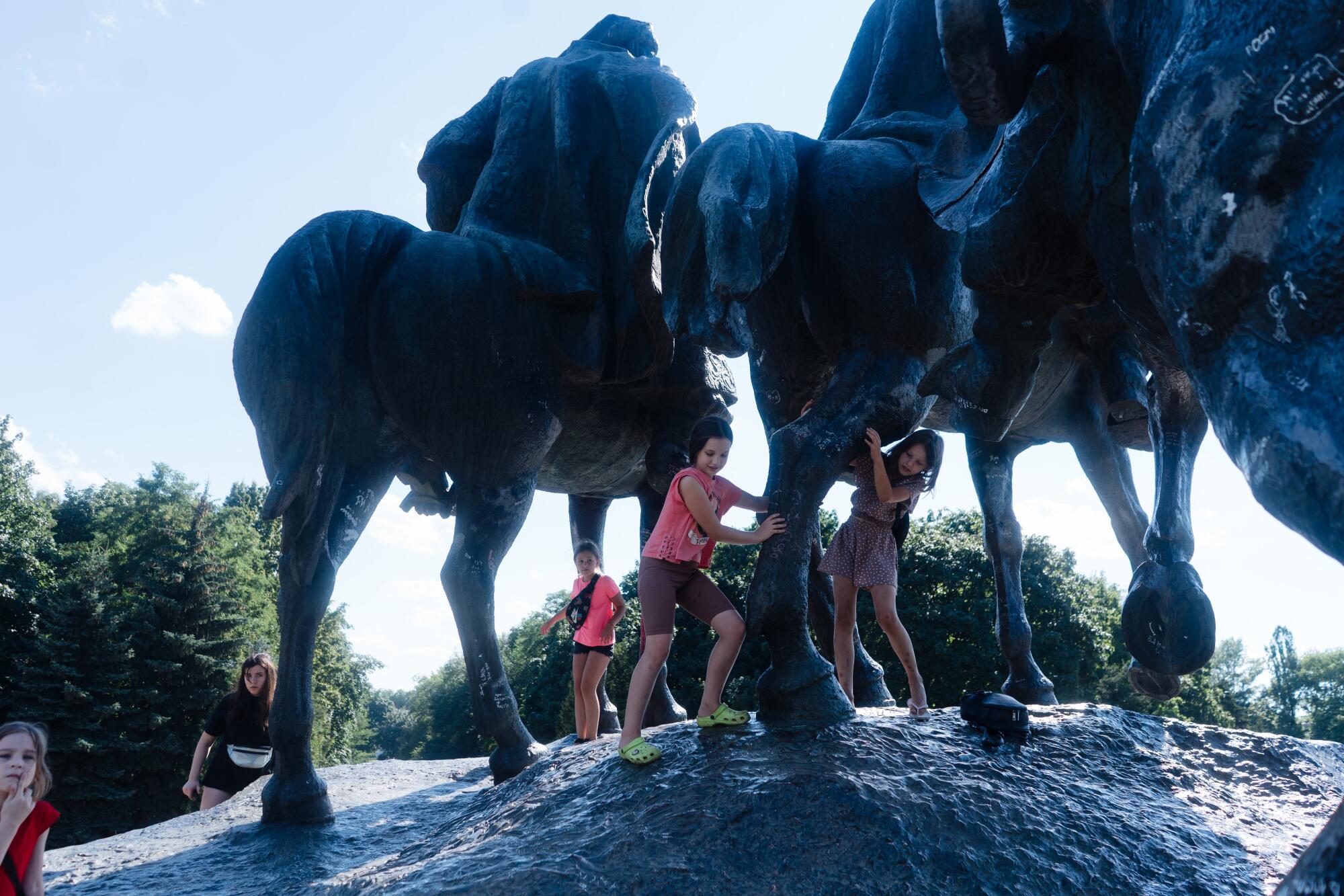 Children play under a sculpture of people on horseback