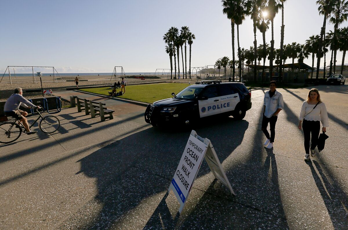 An officer in a police cruiser tells beachgoers Saturday to clear the oceanfront area in Santa Monica, which is closed to enforce social distancing because of the coronavirus pandemic.