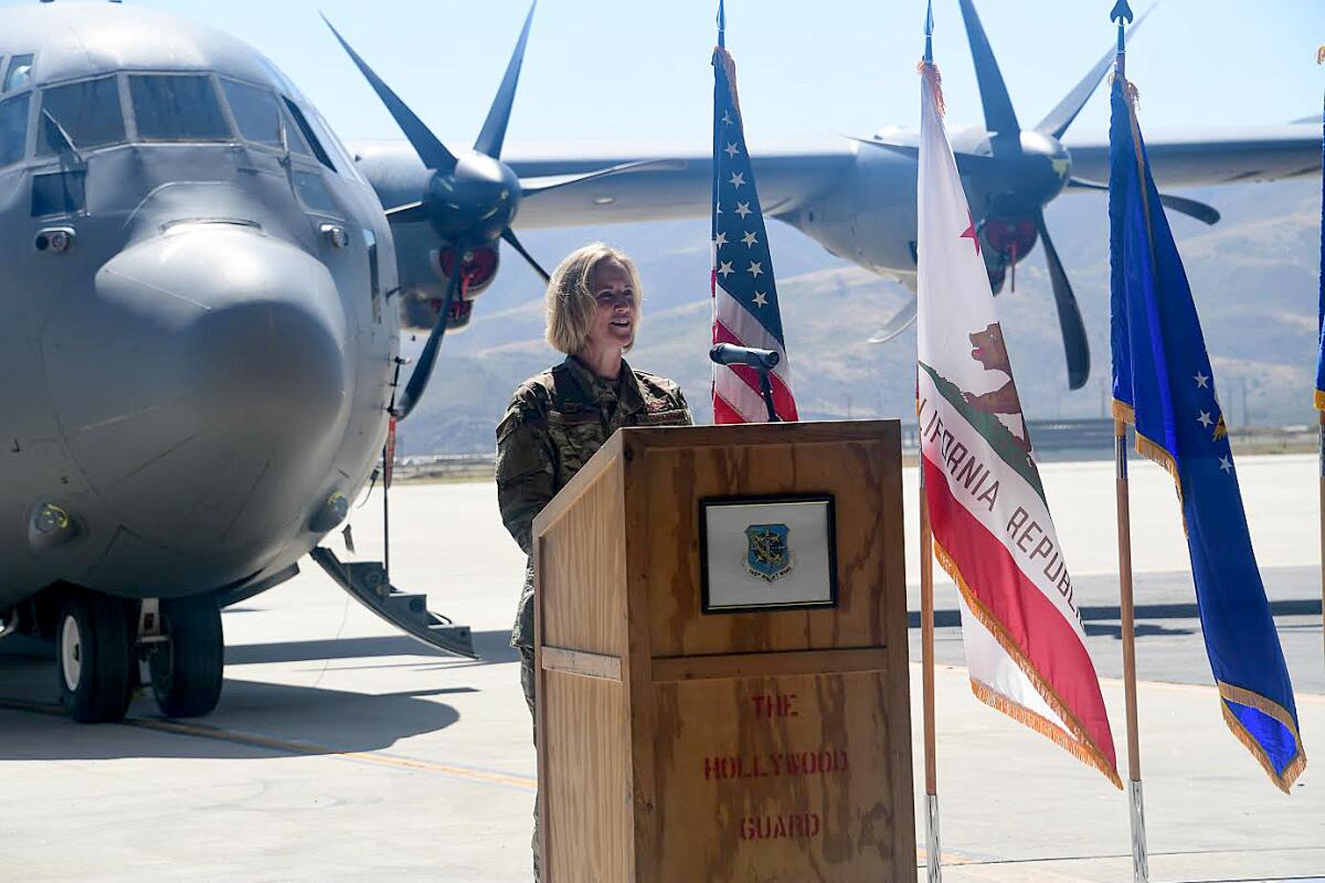 Lisa Nemeth speaks at a lectern before flags and a plane 