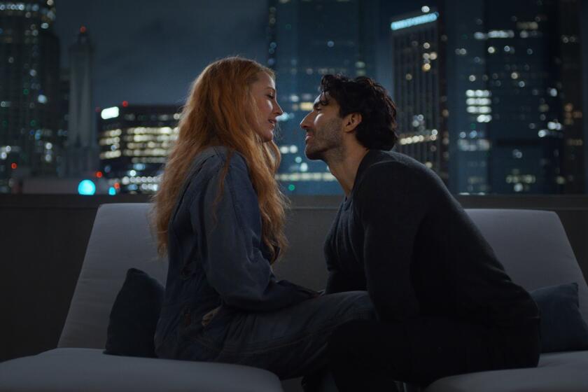 Blake Lively and Justin Baldoni leaning in for a kiss on a couch on a rooftop overlooking a city skyline