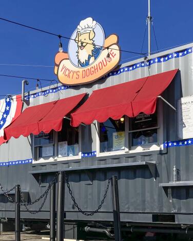 A sign with a cartoon puppy wearing a chef's hat and "Vicky's Doghouse" on a hot dog bun sits above the order window. 