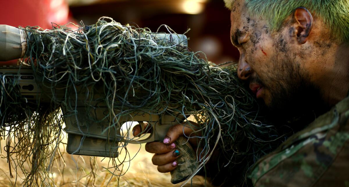 A sniper in camouflage, with painted fingernails and dyed hair.