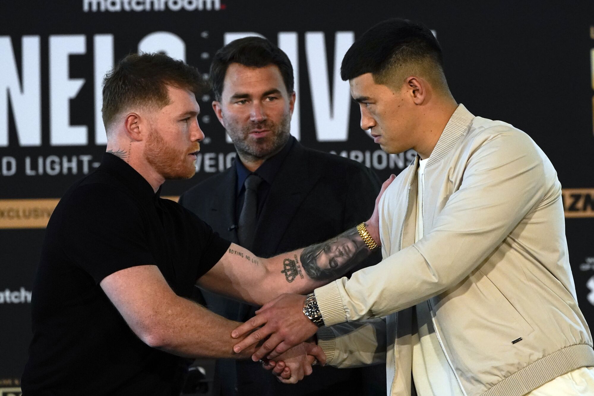 Canelo Álvarez, left, shakes hands with boxer Dmitry Bivol as promoter Eddie Hearn looks on during a weigh-in