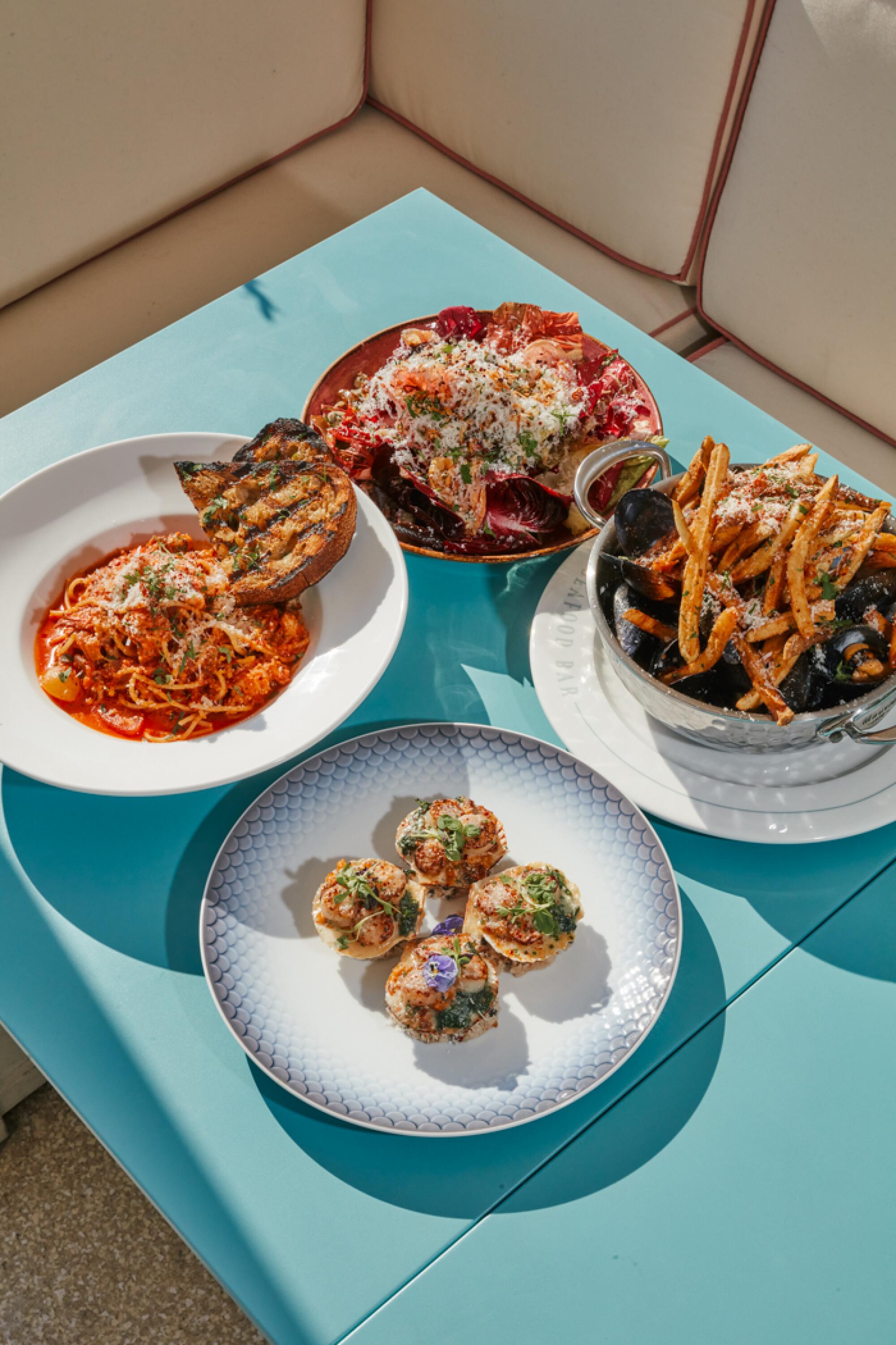 Four plates of food on a turquoise tabletop outside on a restaurant patio.