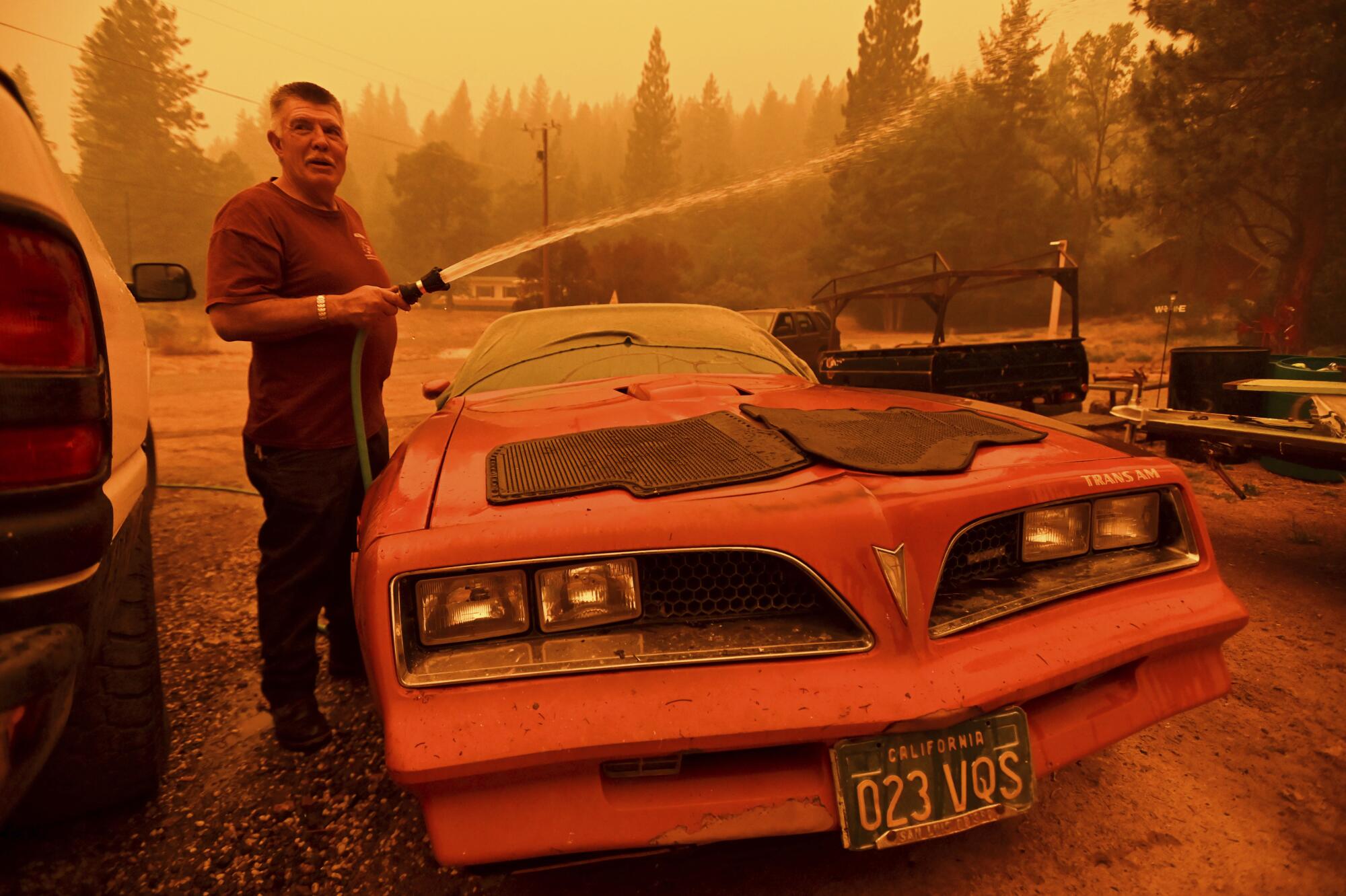 William Deal wets down his 1977 Trans Am as the Dixie fire approaches Crescent Mills in Plumas County, Calif.