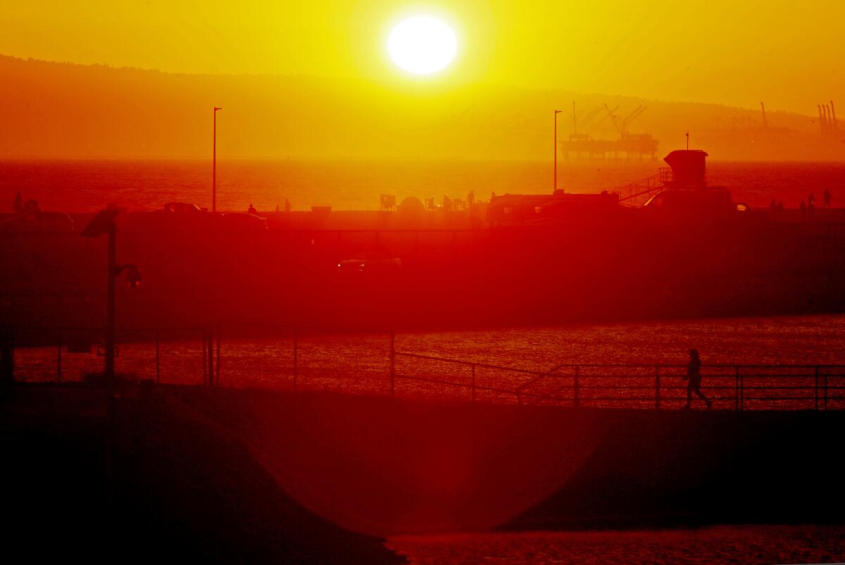 The sun glows as it sets amid haze over ocean and hills.