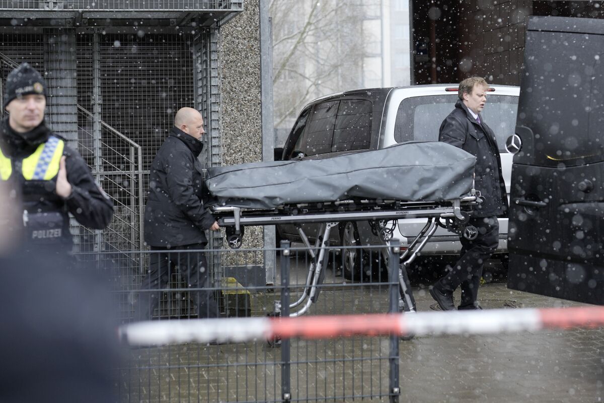A body in a bag is being carried on a stretcher out of a building by two men.