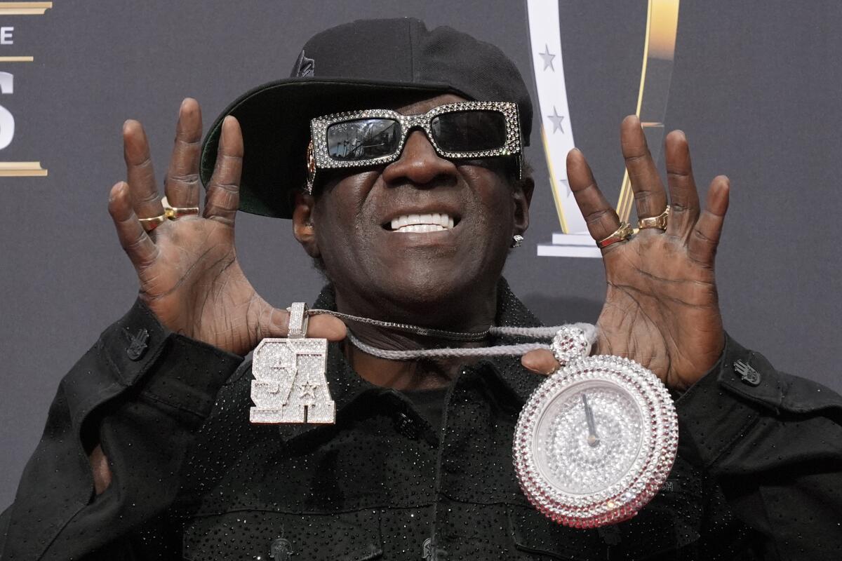 A man wearing sunglasses hold up a diamond chain and clock
