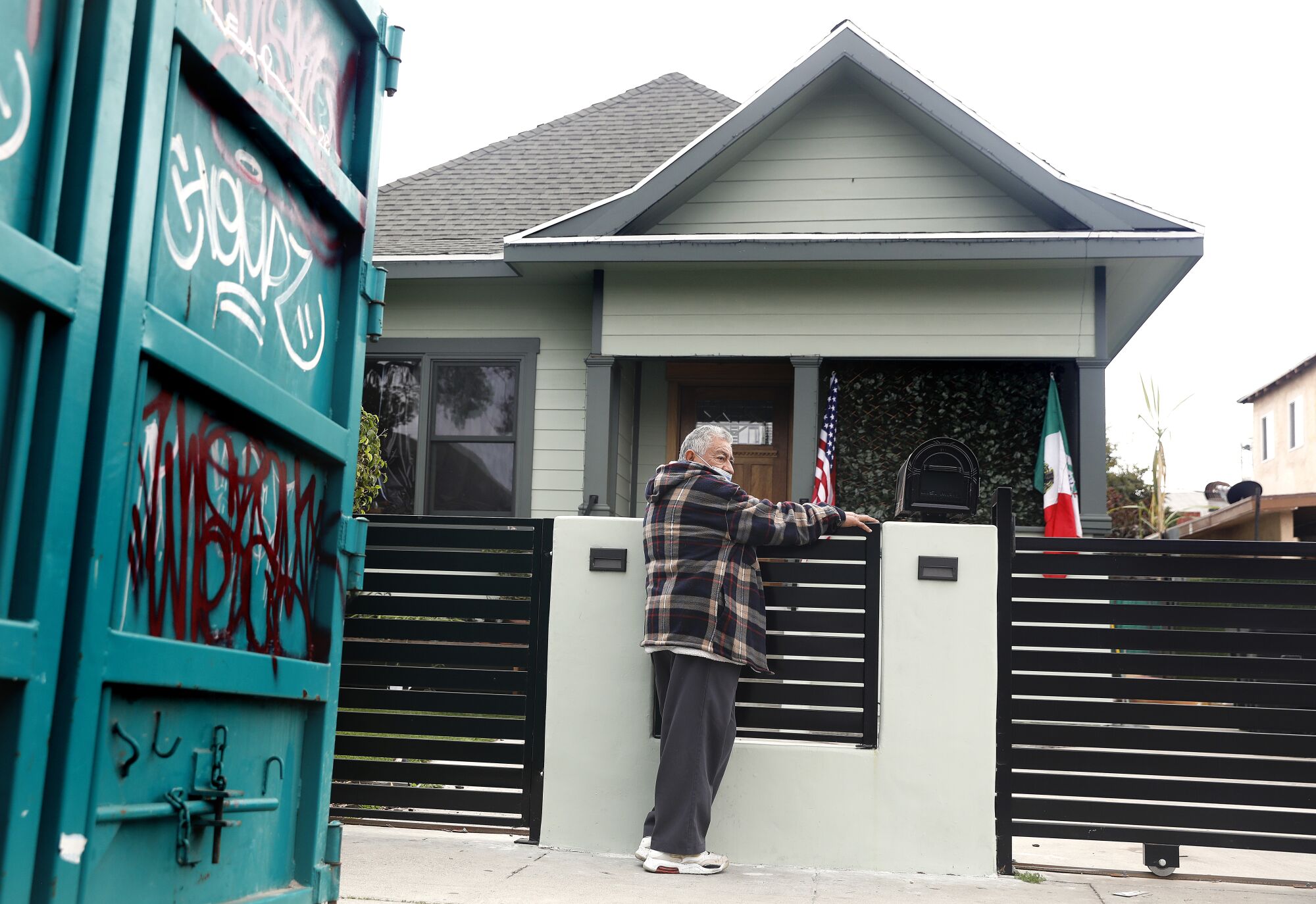 Un homme se tient devant une maison affichant des drapeaux américains et mexicains.