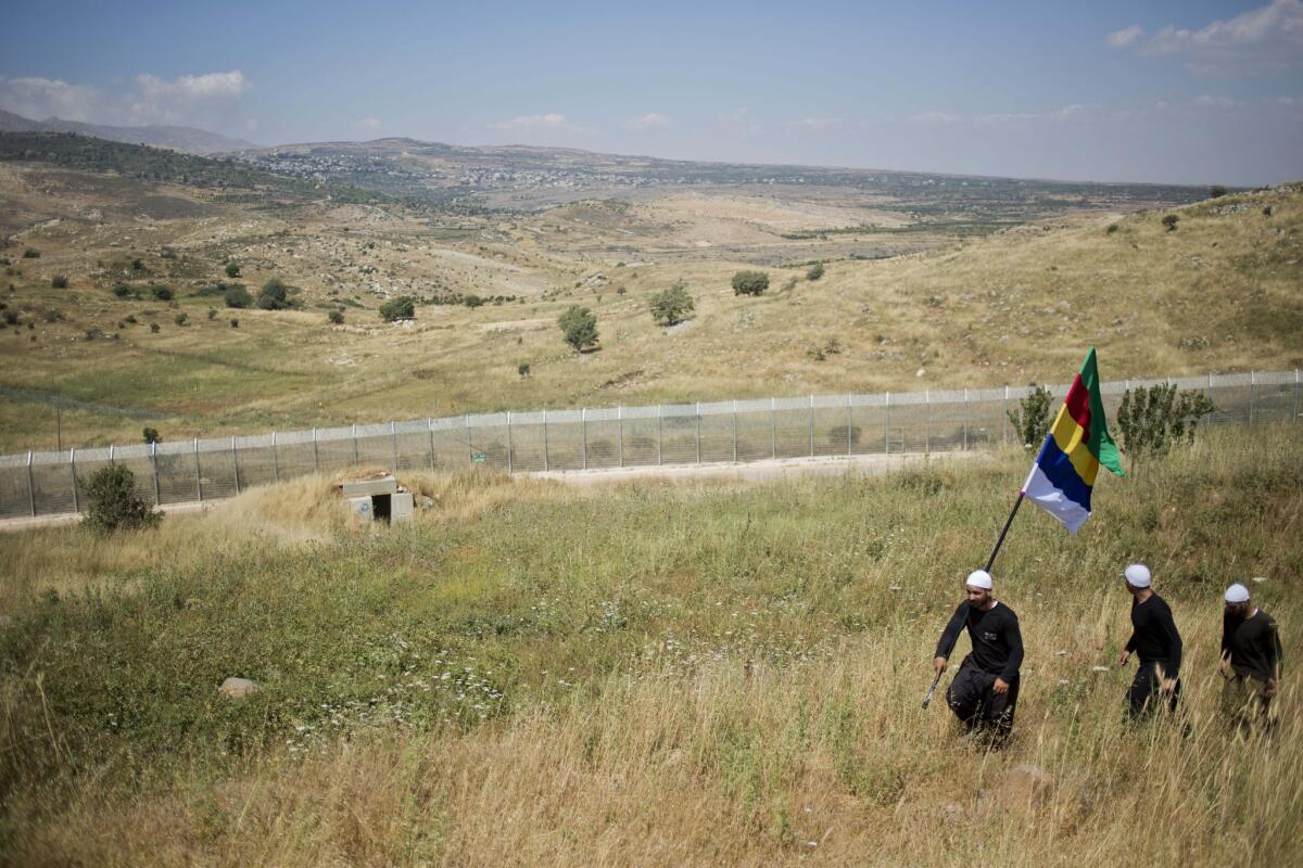 A member of the Druze minority carries the Druze flag as several men walk near the border with Syria in the Israeli-controlled Golan Heights.