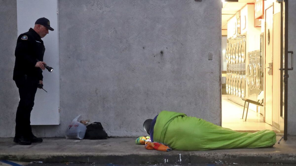 A Costa Mesa officer makes contact with a homeless man sleeping at the rear entrance of a laundromat during the 2019 Point in Time count. The most recent numbers from the count show about 7,000 homeless individuals live in Orange County.