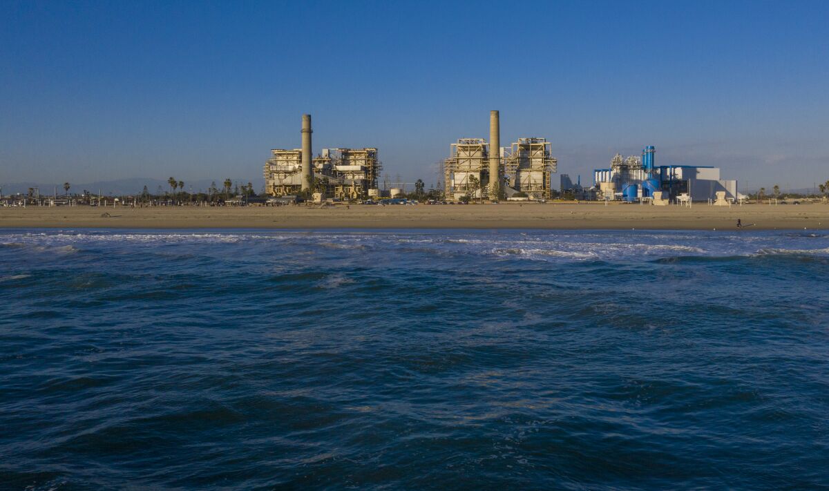 A view of three buildings at a power-generating station, with the ocean in the foreground. 