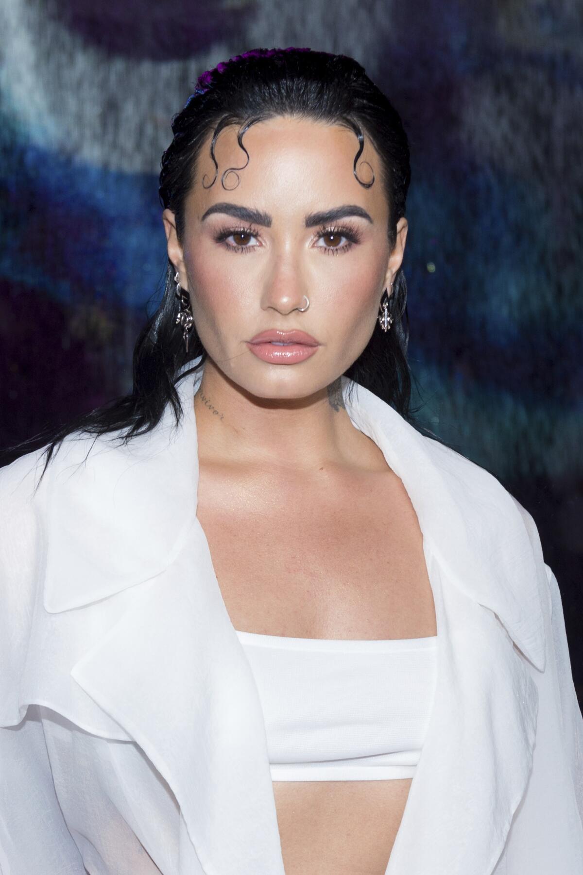 Demi Lovato wears a white bralette and shirt as she poses for photos at a red carpet event