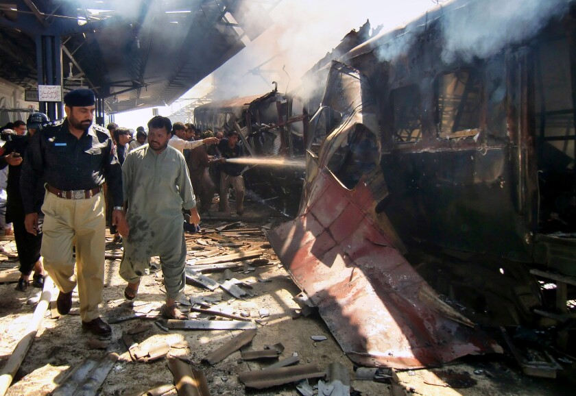 A police officer investigates as firefighters try to extinguish the flames after a train bombing in Pakistan's southwestern province of Baluchistan.