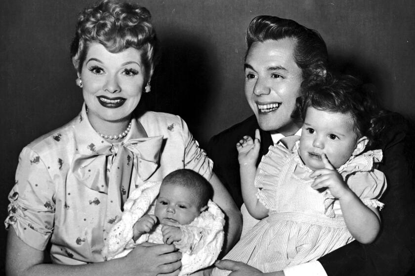 Lucille Ball and her husband, Desi Arnaz, laugh and smile while holding their two children, Desi Jr. and Lucie. 