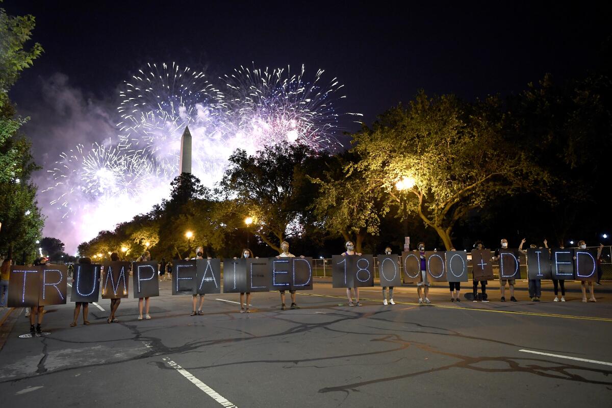 Demonstrators stand with signs as fireworks go off at the Washington Monument at the conclusion of the Republican convention.