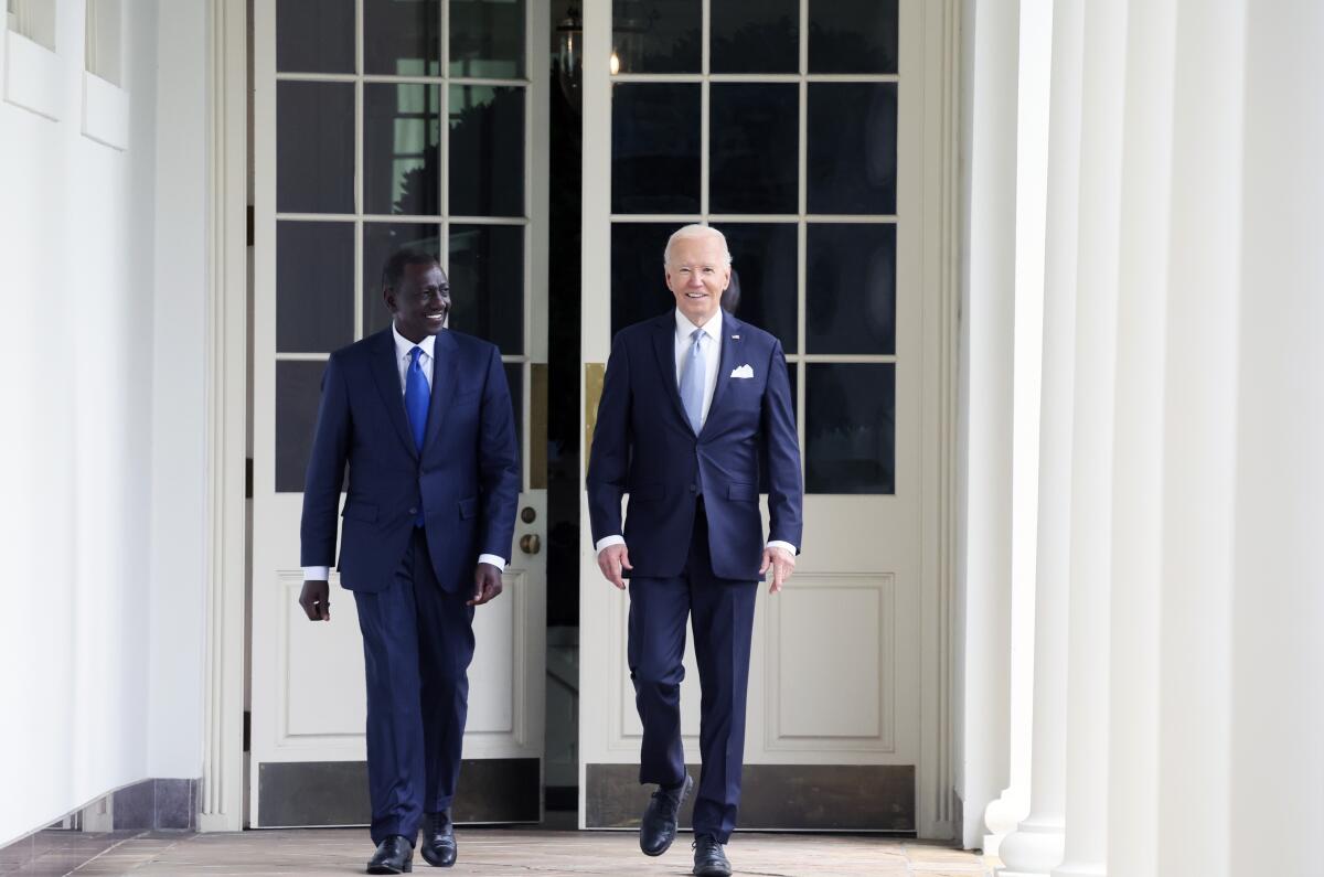 President Biden and Kenyan President William Ruto walk in front of two tall doors outside.