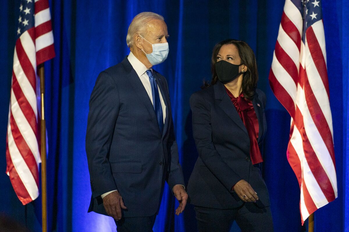 Joe Biden and Kamala Harris walk onto a stage in front of a blue curtain and two U.S. flags