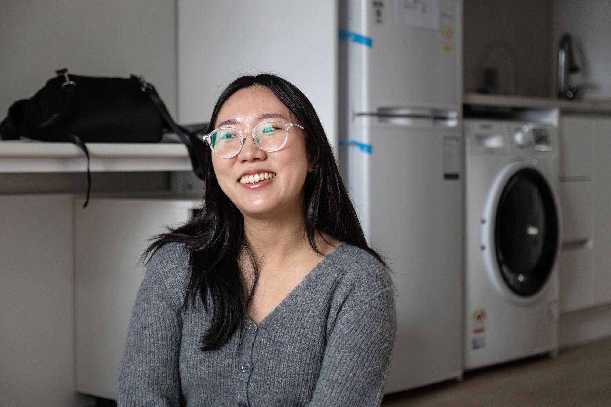 Kim Do-yeon sits and smiles in a room with appliances in the background.