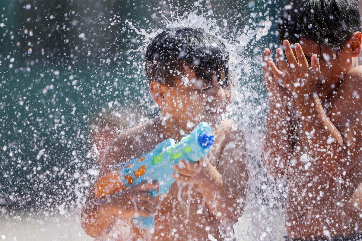 A child holds a water gun as he and another child get splashed in a play area.