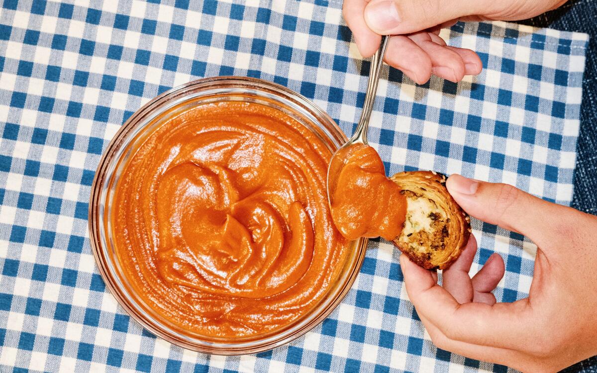 Spooning tomato sauce from a bowl onto a sausage roll