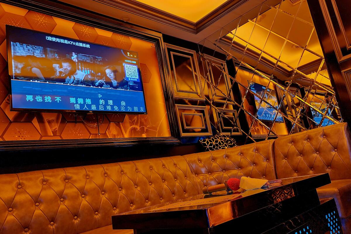 A gold-tinted private room at Spark Karaoke with a tufted banquette and a TV screen displaying lyrics.