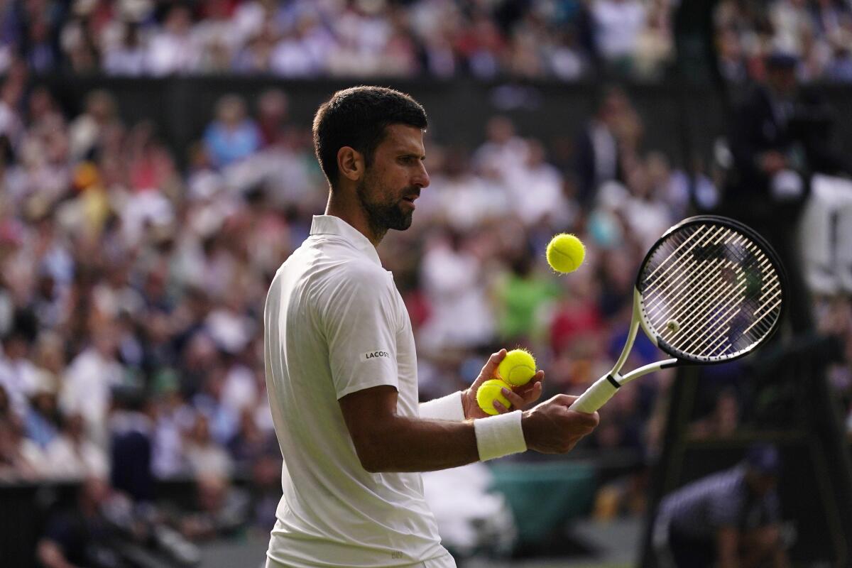 Novak Djokovic holds two tennis balls and a racket while one ball is in the air.