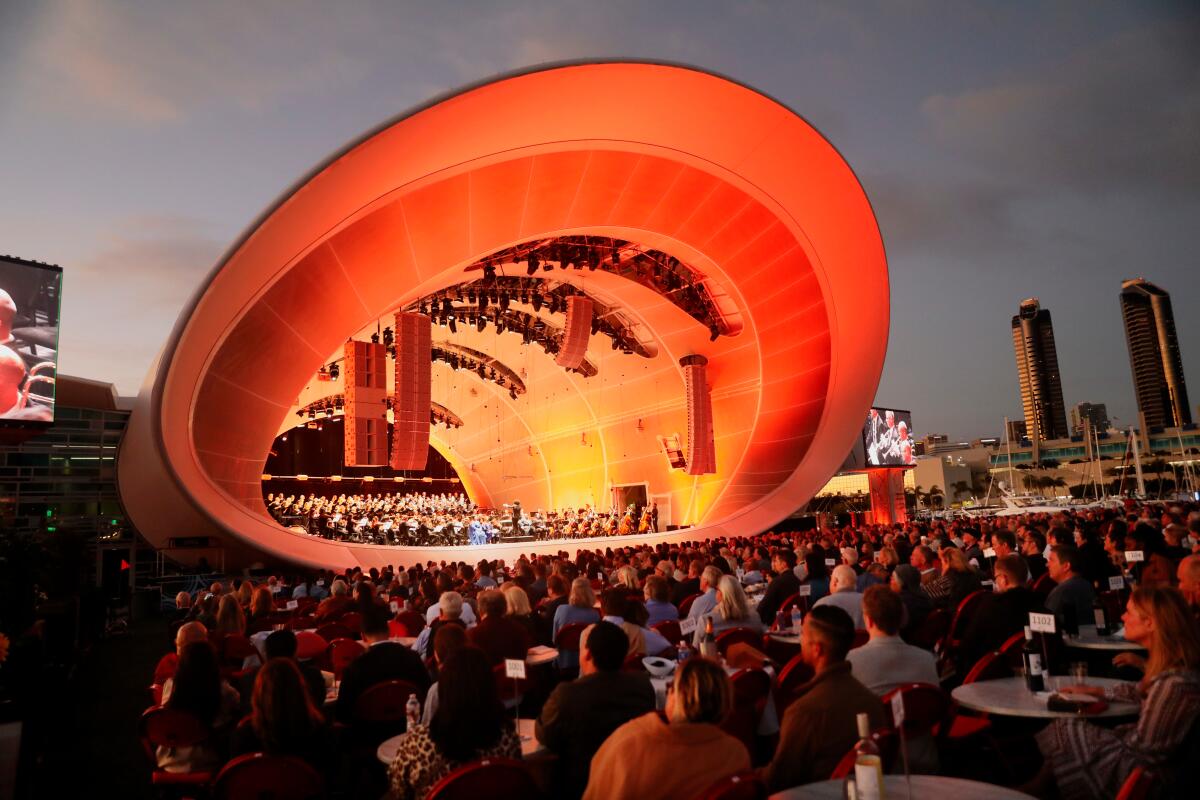 A band shell on a pier park in San Diego is bathed in orange light at dusk.