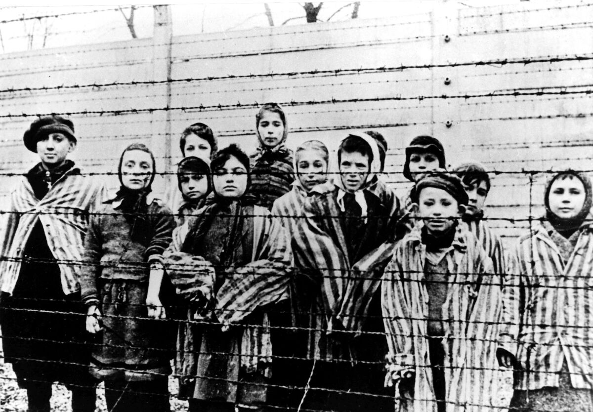 A black-and-white photo of a group of children standing behind barbed wire fencing 