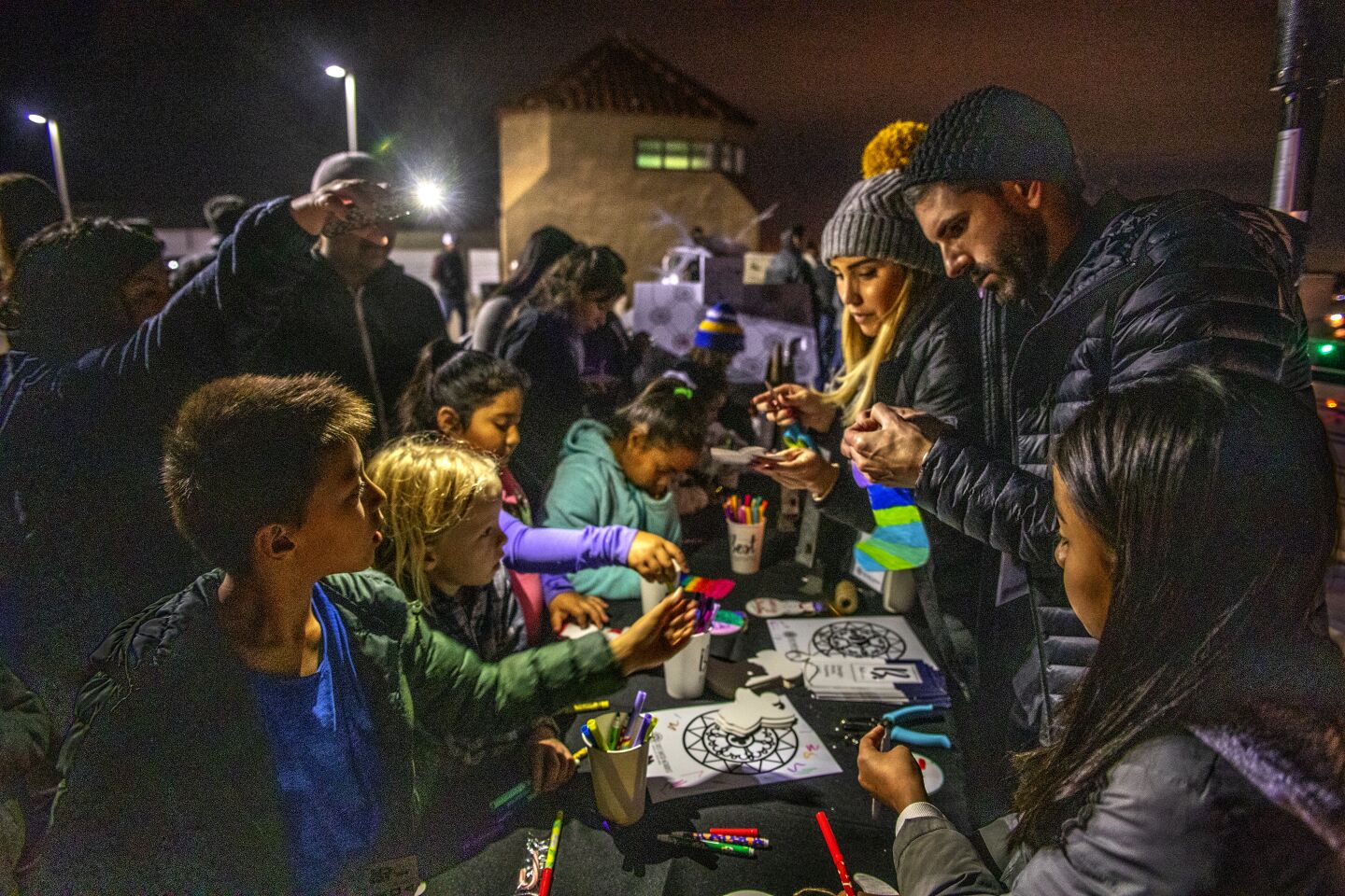 Lauren Bergmann and Kyle Landig craft Christmas ornaments for their young audience at the art project table during Sunday night's Shine Bright festivities in Costa Mesa.