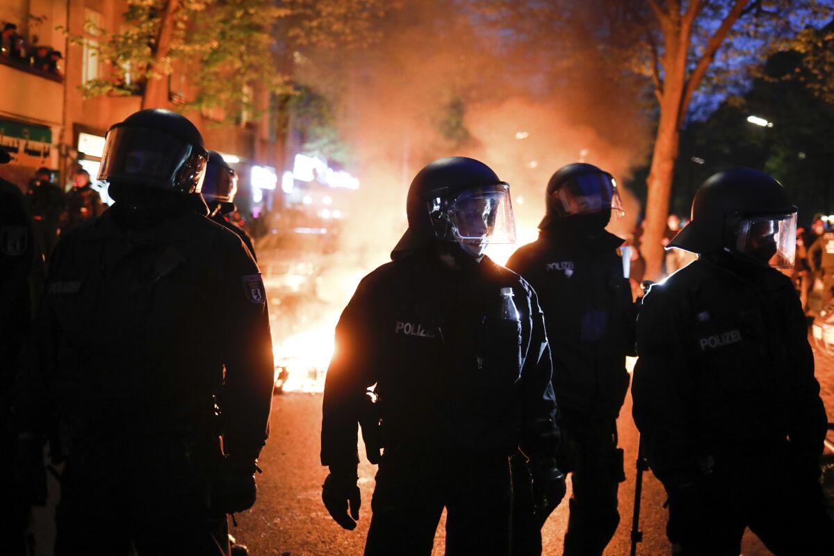 Police in riot gear are silhouetted against flames on a city street.