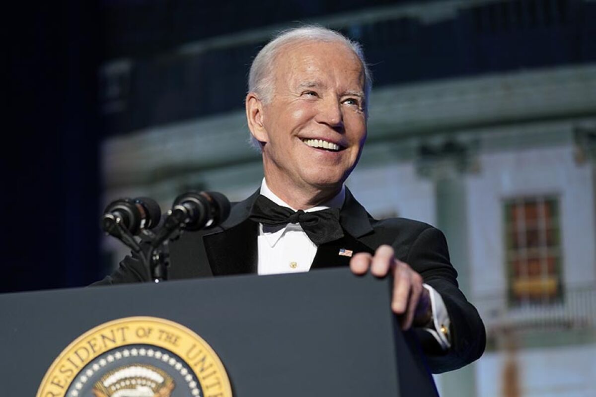 President Biden smiles standing before microphones at a lectern with the presidential seal