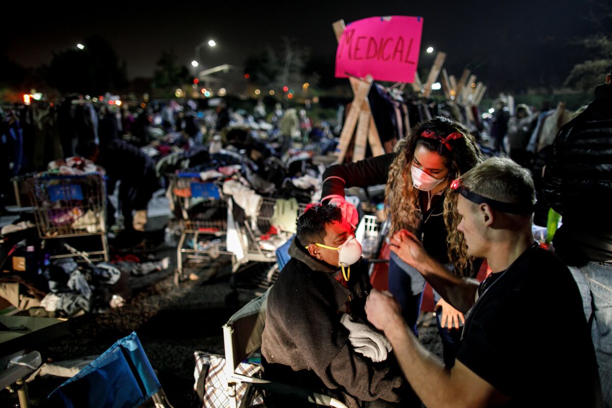 Crane Ruelas and Vanessa Ruelas, volunteers at a makeshift medical station, help a displaced resident with an open wound at a tent city where evacuees of the Camp fire have gathered in Chico.