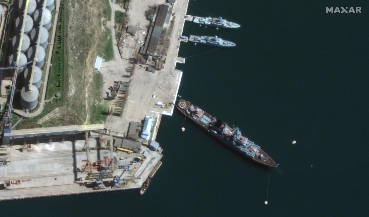An aerial view of a ship sitting at an angle in port near two smaller ships