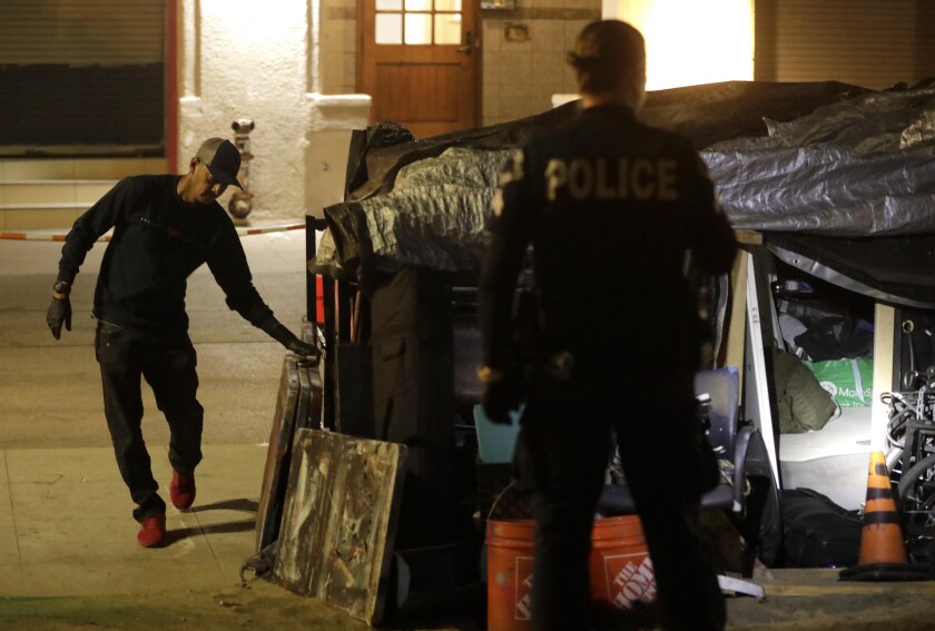 An officer watches a homeless artist pack up his belongings in Venice on July 8.