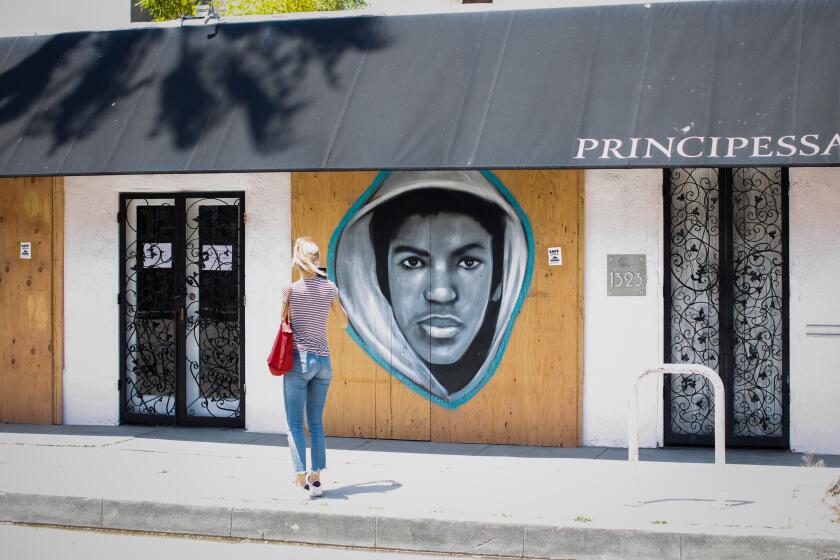VENICE, CA - JUNE 04: A woman stops to photograph a portrait of Treyvon Martin, the 17-year-old who was killed by George Zimmerman in Florida in 2012, claiming self-defense, made by Venice artist Jules Muck, known as MuckRock, on Abbot Kinney Boulevard, in Venice, CA, on Thursday, June 4, 2020. In the aftermath of George Floyd's killing, peaceful protests were marred by looting. To forestall the possibility of looting, many business owners preemptively boarded up their windows, which gave MuckRock canvases for work honoring the lives of those lost to brutality.(Jay L. Clendenin / Los Angeles Times)