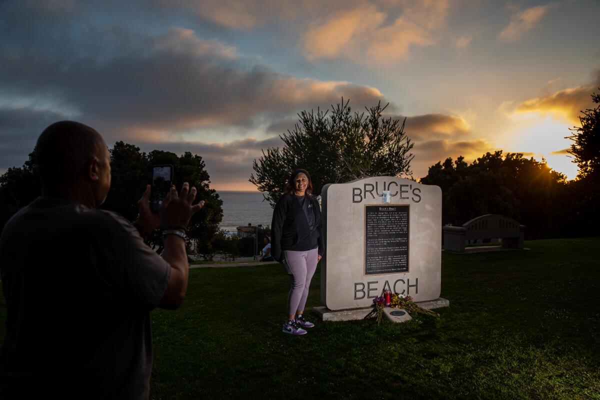 A woman poses by a large stone memorial sign while a man takes her photo