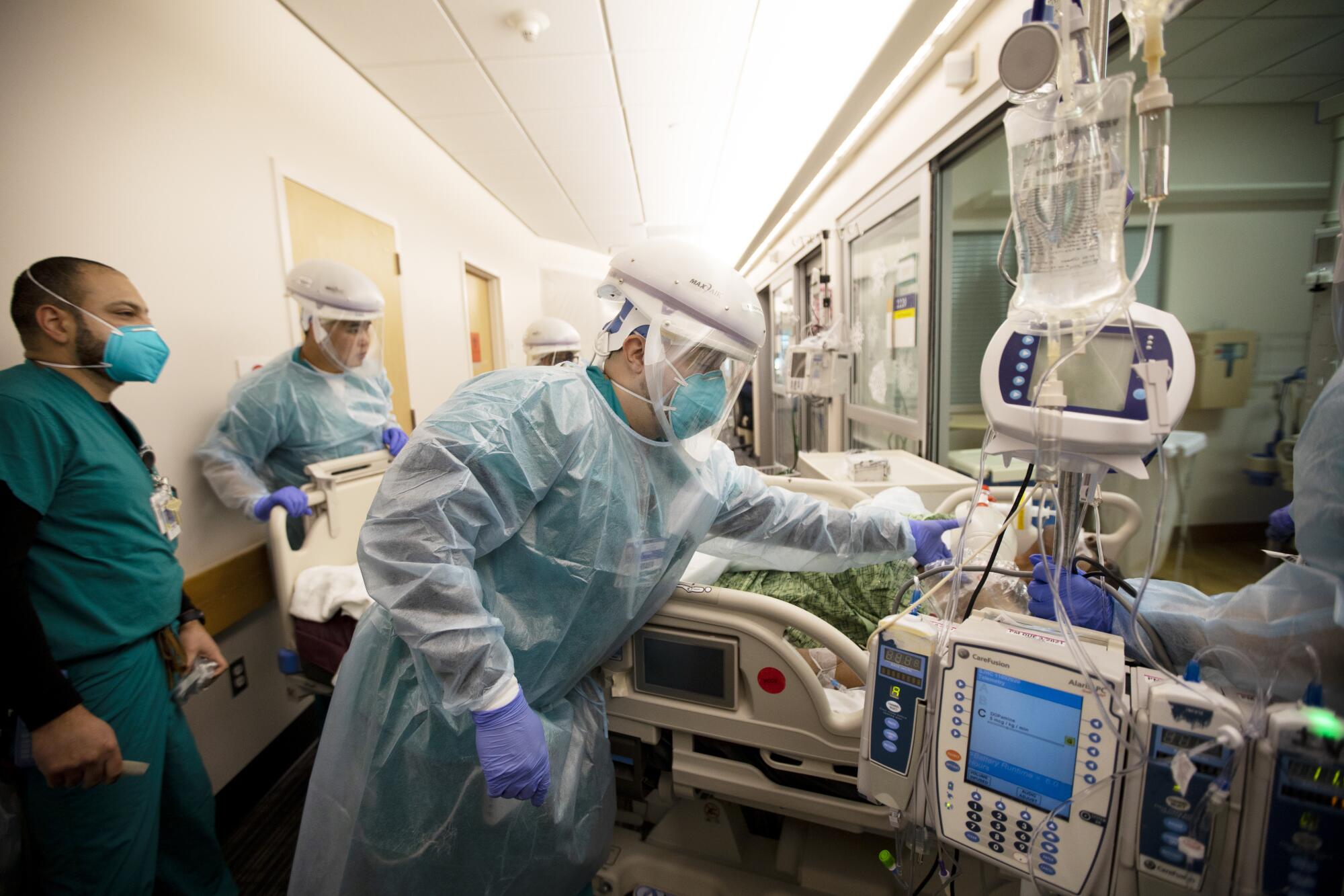 Hospital staff in protective gear move a gurney and monitors.