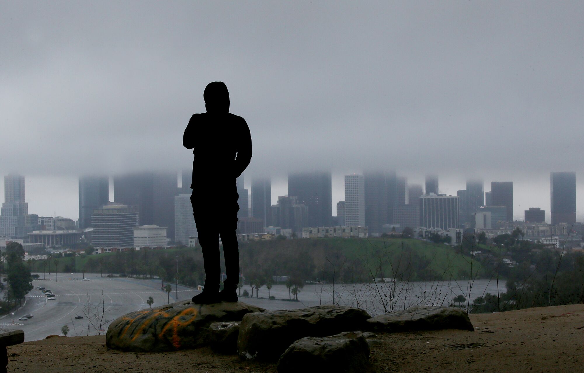 A man watches rain clouds blanket the skyline of downtown Los Angeles.
