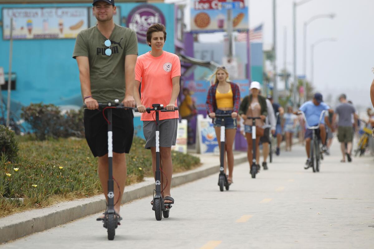 People ride the boardwalk on scooters in Pacific Beach.