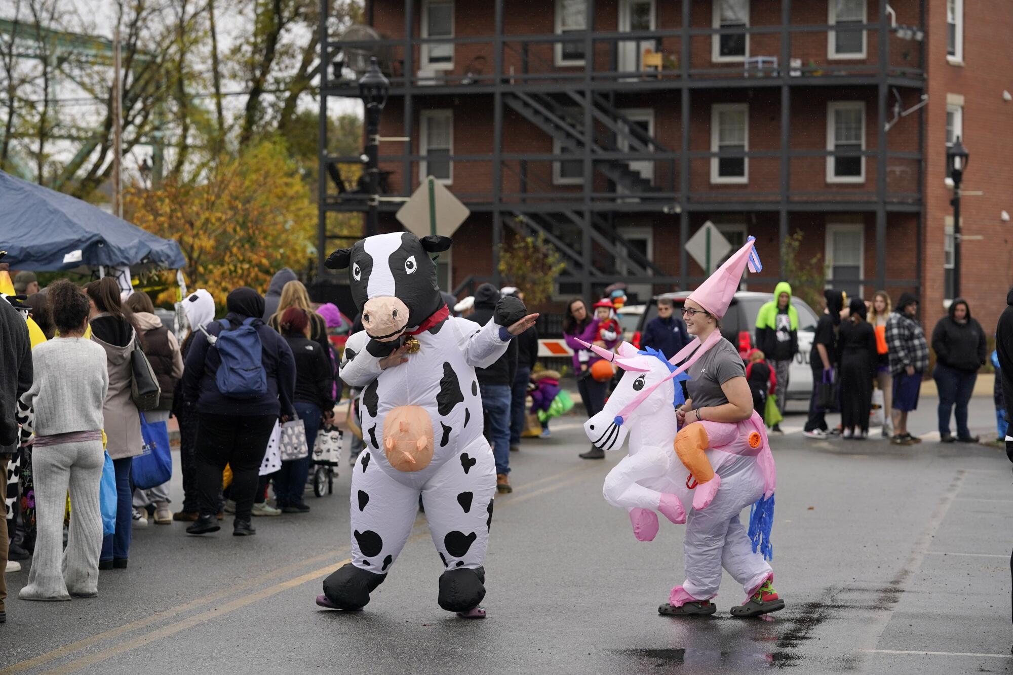 People dressed up as a cow and a unicorn rider dance next to a crowd in a street