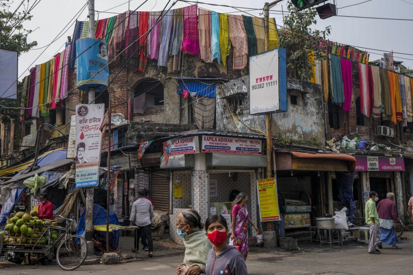 Varias personas, con mascarilla para protegerse contra el coronavirus, pasan por delante de una fábrica de tinte de telas en Calcuta, India, el 26 de enero de 2022. (AP Foto/Bikas Das)