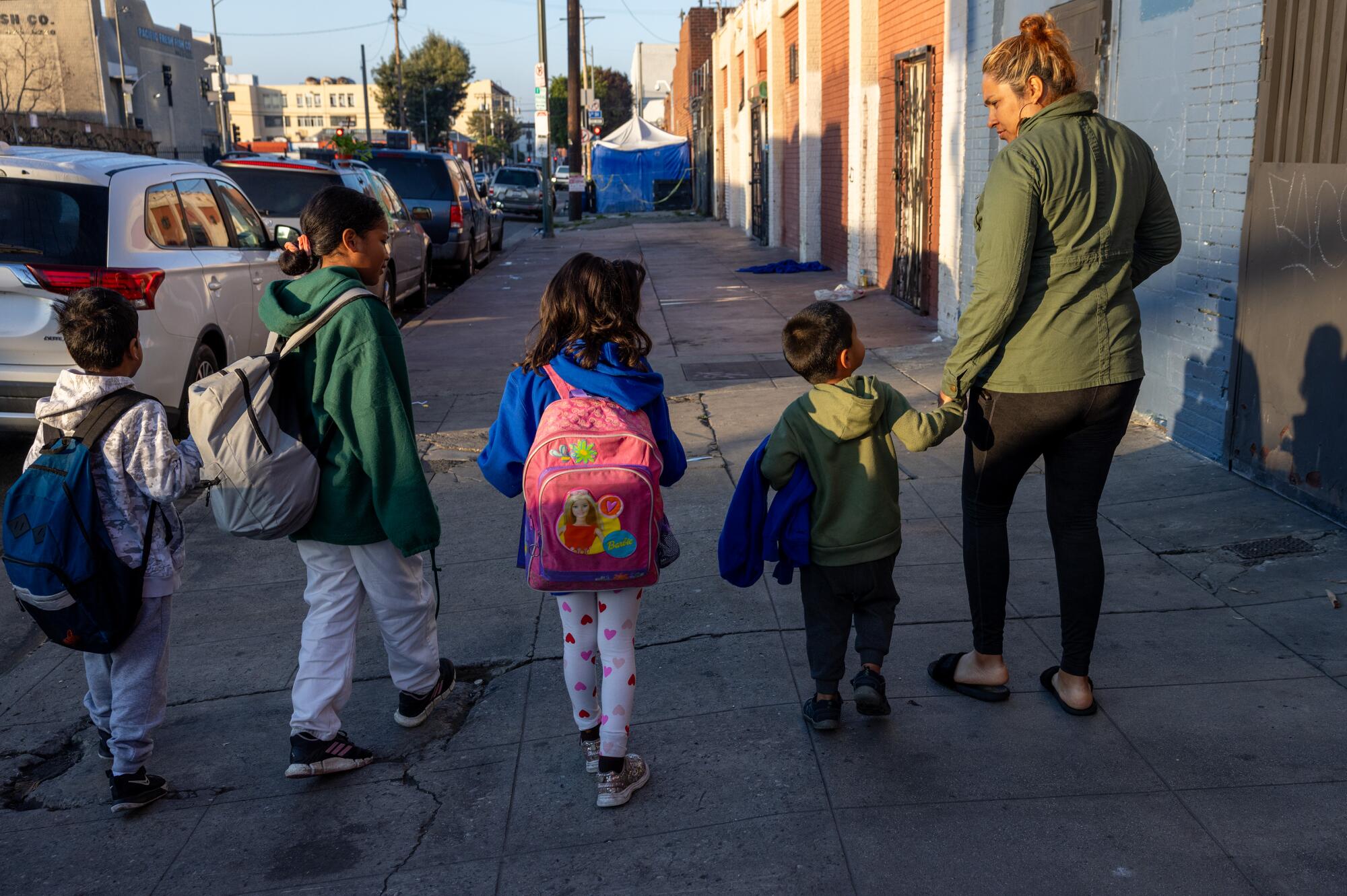 A woman walks with four children on a sidewalk.