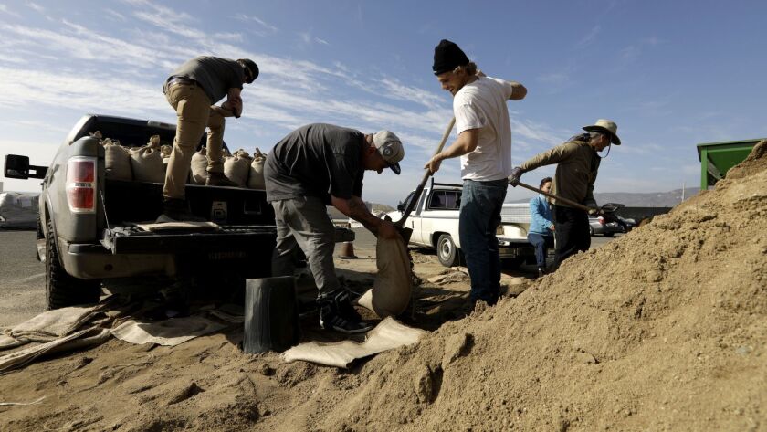 Winston Smedley, second from left, holds a sandbag as Henry Jenkinson fills it with sand, and Alex Halley, far left, waits to load it onto the truck. The three work for a general contracting company in Malibu and were preparing for the rain.