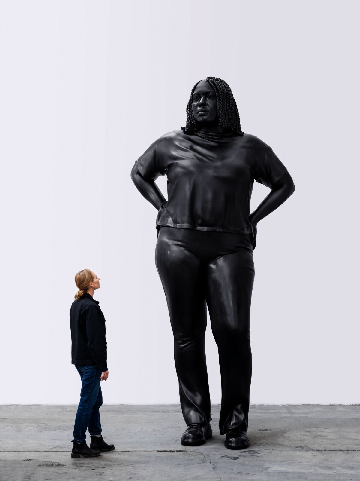 A museum-goer looking up at a huge bronze sculpture of a woman.