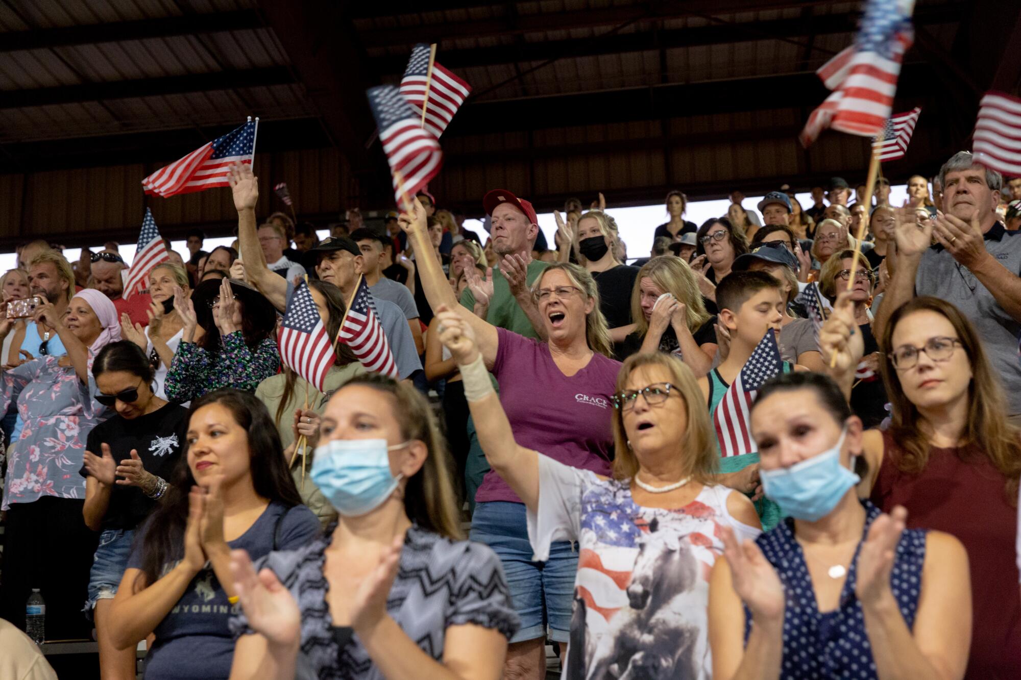 Many people in stands outdoors waving and clapping.