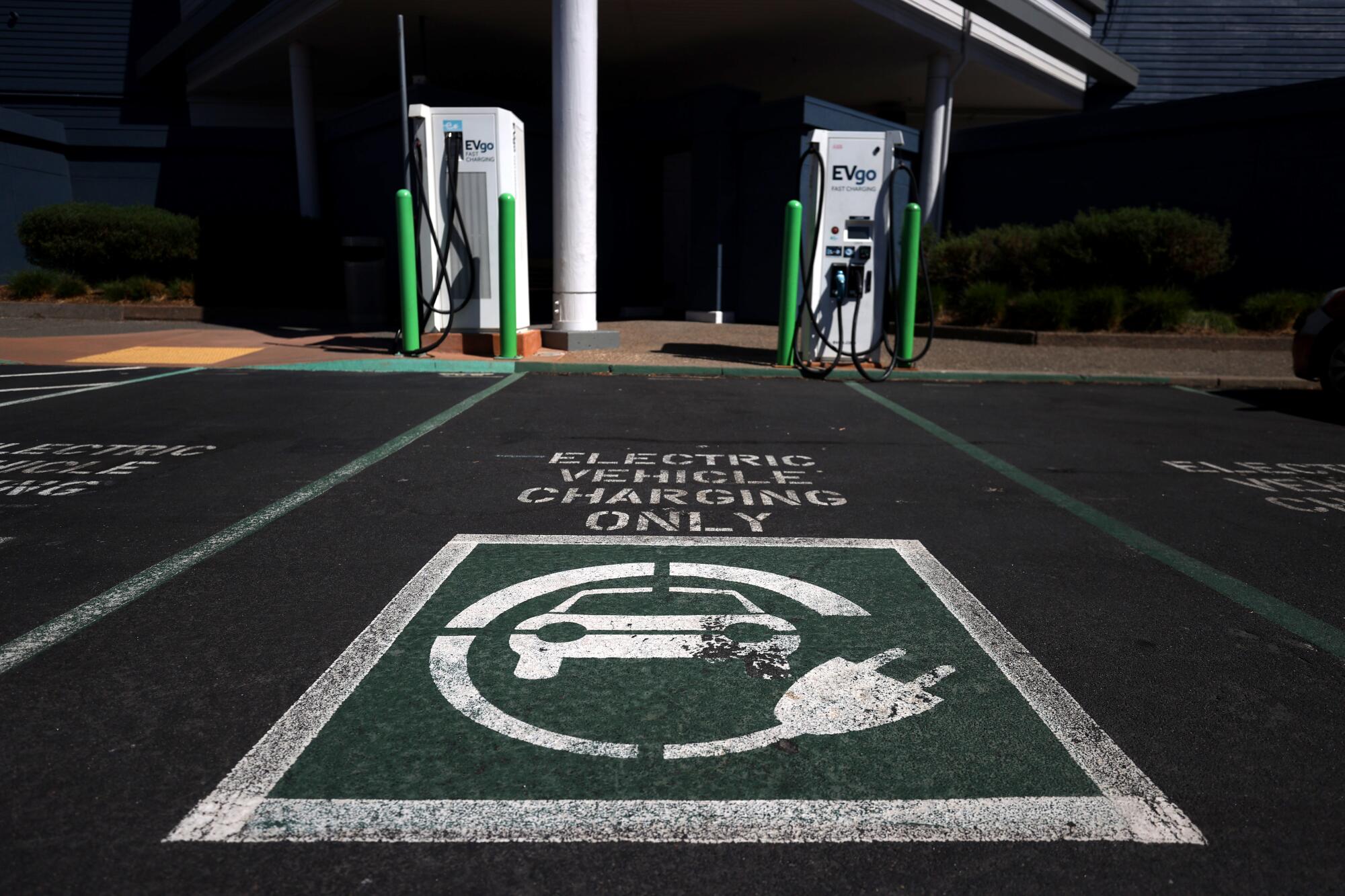 A parking spot labeled "Electric vehicle charging only" with an EV graphic, in front of two charging stations in a dark lot